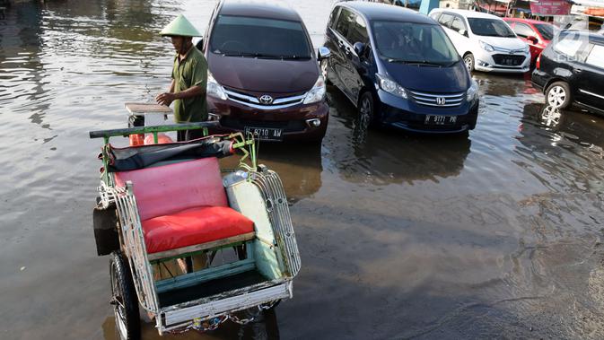 Seorang pria berada di dekat becak di jalan Yos Sudarso Semarang yang terendam banjir di kawasan Pelabuhan Tanjung Emas (24/4). (Liputan6.com/Gholib)