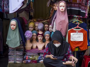 Seorang pedagang menggunakan telepon seluler pintarnya sambil menunggu pelanggan di sebuah kios pinggir jalan di Jakarta pada 30 Juni 2025. (BAY ISMOYO/AFP)