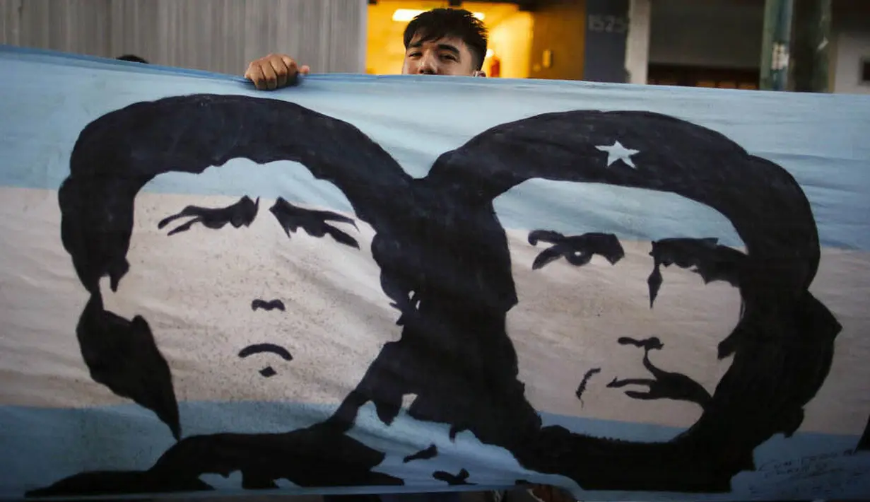 Seorang fans membentangkan bendera bergambar Diego Maradona dan Ernesto "Che" Guevara di depan Rumah Sakit di La Plata, Argentina, Selasa (3/11/2020). Sejumlah fans Argentina berkumpul di depan rumah sakit untuk memberi dukungan kepada sang legenda. (AP/Natacha Pisarenko)