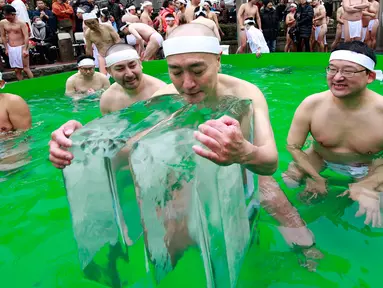 Seorang peserta mandi air dingin memeluk balok es di Teppozu Inari Shinto Shrine di Tokyo, Jepang (8/1). Acara tersebut merupakan ritual musim dingin yang diyakini dapat menjaga kesehatan mereka. (AP Photo/Shizuo Kambayashi)