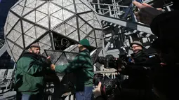 Awak media melihat pekerja menyelesaikan pemasangan bola kristal di atas sebuah gedung di Times Square, New York, Kamis (27/12). Menyaksikan bola kristal raksasa adalah tradisi yang tidak terlewatkan setiap perayaan tahun baru sejak 1907. (AP/Seth Wenig)