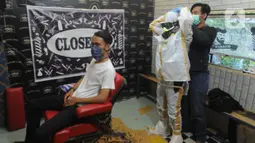 Seorang tukang cukur memakai alat pelindung diri (APD) buatannya sendiri sebelum mencukur pelanggannya di Chemot Barbershop, Ciawi, Bogor, Jawa Barat, Minggu (5/4/2020). (merdeka.com/Arie Basuki)