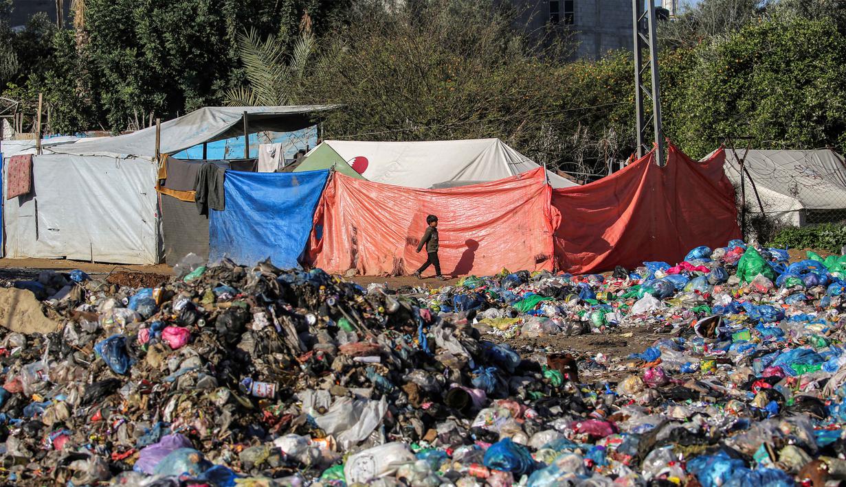 James Elder menyebut situasi ini bukan sekadar kehancuran fisik, melainkan sebuah serangan terhadap masa depan yang telah menghapus kemajuan pendidikan selama bertahun-tahun. Tampak dalam foto, seorang anak laki-laki berjalan melewati tumpukan sampah yang dibuang di dekat tenda-tenda pengungsi yang didirikan di kamp Nuseirat untuk pengungsi Palestina di utara Deir al-Balah, Jalur Gaza tengah pada 29 Januari 2026. (EYAD BABA/AFP)