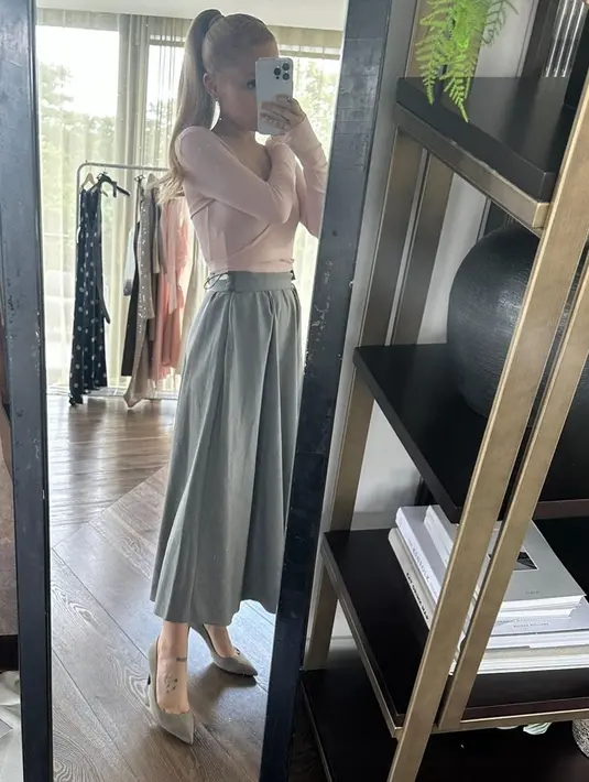 Kesempatan lainnya, Ariana Grande tampil di mirror selfie mengenakan atasan lengan panjang berwarna merah muda, yang dipadu dengan wide-leg pants abu-abu. Rambut blondenya ditata high pony-tail. Foto: Instagram.