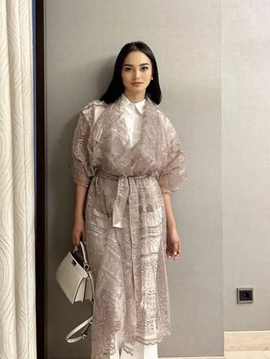 Ririn Ekawati tampil dengan heels putih yang dipadukan dengan kemeja putih dan celana putih di atas outer panjang lace kecokelatannya. Credit: Instagram (@ririnekawati)