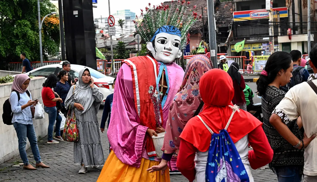 Foto pada 16 Maret 2019 menunjukkan ondel-ondel yang dioperasikan oleh seorang anak untuk mengamen di jalanan Jakarta. Seiring berjalan waktu, ondel-ondel yang dahulu sebagai ikon kesenian Betawi kini mudah ditemui di sejumlah jalan dan gang-gang di antara permukiman warga. (GOH CHAI HIN / AFP)