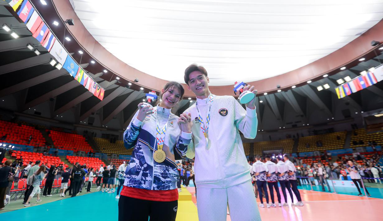 Meski begitu, keduanya tetap fokus memberikan usaha yang terbaik untuk timnas mereka. Tampak dalam foto, pevoli Indonesia Alfin Daniel Pratama (kanan) berfoto bersama dengan kekasihnya yang juga penerjemah Timnas voli putra Thailand, McEntee Catherine, di di Stadion Indoor Hua Mak, Jumat (19/12/2025). (Bola.com/Bagaskara Lazuardi)