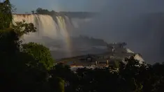 Pengunjung berjalan di sepanjang jalan setapak saat pelangi muncul di depan sebagian pemandangan Air Terjun Devil's Throat, bagian dari sistem Air Terjun Iguazu di Sungai Iguazu di Taman Nasional Iguacu, Negara Bagian Parana, dekat Foz do Iguacu di Brasil selatan yang berbatasan dengan Argentina, saat matahari terbenam pada 21 Mei 2024. (Mariana SUAREZ / AFP)