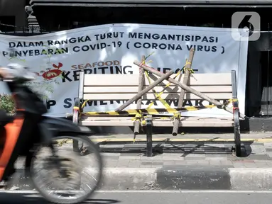 Pengendara melintasi bangku trotoar yang disegel garis pembatas dan ditutupi bambu di kawasan Rawamangun, Jakarta, Minggu (3/5/2020). Bangku trotoar di sepanjang jalan Rawamangun disegel untuk mencegah kerumunan warga sebagai upaya memutus rantai penyebaran COVID-19. (merdeka.com/Iqbal S. Nugroho)