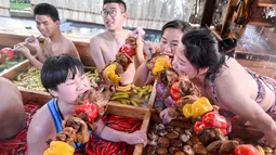 Pengunjung menyantap daging tusuk sambil menikmati berendam di kolam air panas berbentuk hot pot di sebuah hotel di Hangzhou, China, Minggu (27/1). Pemandian air panas itu dirancang untuk mempromosikan gaya hidup sehat menjelang Tahun Baru Imlek (STR/AFP)
