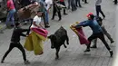 Sejumlah pria melemparkan jubah mereka pada banteng muda dalam acara lari dikejar banteng di Pillaro, Ekuador, 4 Agustus 2018. Dalam acara ini, lusinan banteng dilepas dan berlari menabraki para pengunjung yang memadati jalan. (AP/Dolores Ochoa)