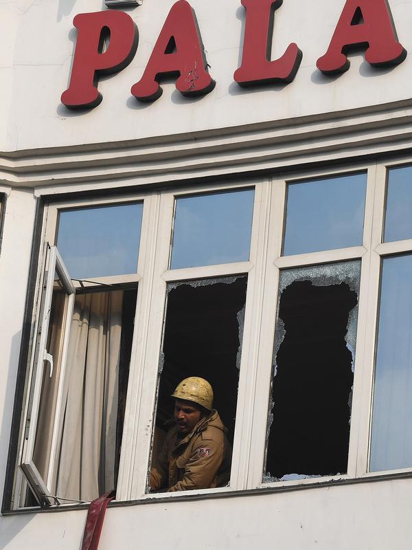 Petugas pemadam kebakaran melihat keluar jendela yang rusak setelah kebakaran Hotel Arpit Palace di Distrik Karol Bagh, New Delhi, Selasa (12/2). Sejauh ini belum diketahui penyebab munculnya api yang memicu kebakaran tersebut. (Prakash SINGH / AFP)