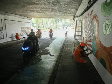 Petugas Penanganan Prasarana dan Sarana Umum (PPSU) menyelesaikan lukisan mural pada tembok kolong Semanggi, Jakarta, Jumat (7/7/2023). Pembuatan mural tersebut guna mempercantik kawasan tersebut yang selalu dilewati pengguna jalan. (Liputan6.com/Faizal Fanani)