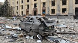 Sebuah mobil yang terbakar terlihat di depan gedung Balai Kota yang rusak di Kharkiv pada 1 Maret 2022. Alun-alun pusat kota terbesar kedua Ukraina, Kharkiv, ditembaki oleh pasukan Rusia -- menghantam gedung pemerintahan lokal -- kata gubernur Oleg Sinegubov. (Sergey BOBOK / AFP)