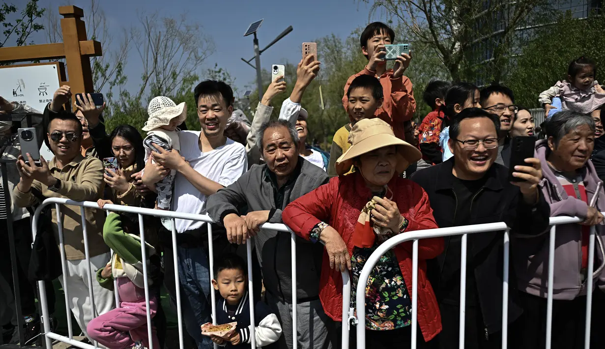 Para penduduk menyaksikan perlombaan lari half marathon yang diikuti oleh robot humanoid di Beijing, China, Sabtu (19/04/2025). (AFP/Pedro Pardo)