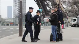 Polisi memeriksa dokumen warga saat lockdown di depan Menara Eiffel, Paris, Prancis, Rabu (18/3/2020). Prancis mengerahkan puluhan ribu polisi untuk berpatroli selama lockdown akibat virus corona COVID-19. (Ludovic MARIN/AFP)