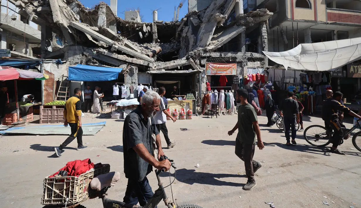 Warga Palestina berjalan melewati bangunan yang hancur di pasar darurat di kamp pengungsi Nuseirat, yang terletak di bagian tengah Jalur Gaza, pada 15 Oktober 2025. (Eyad BABA/AFP)