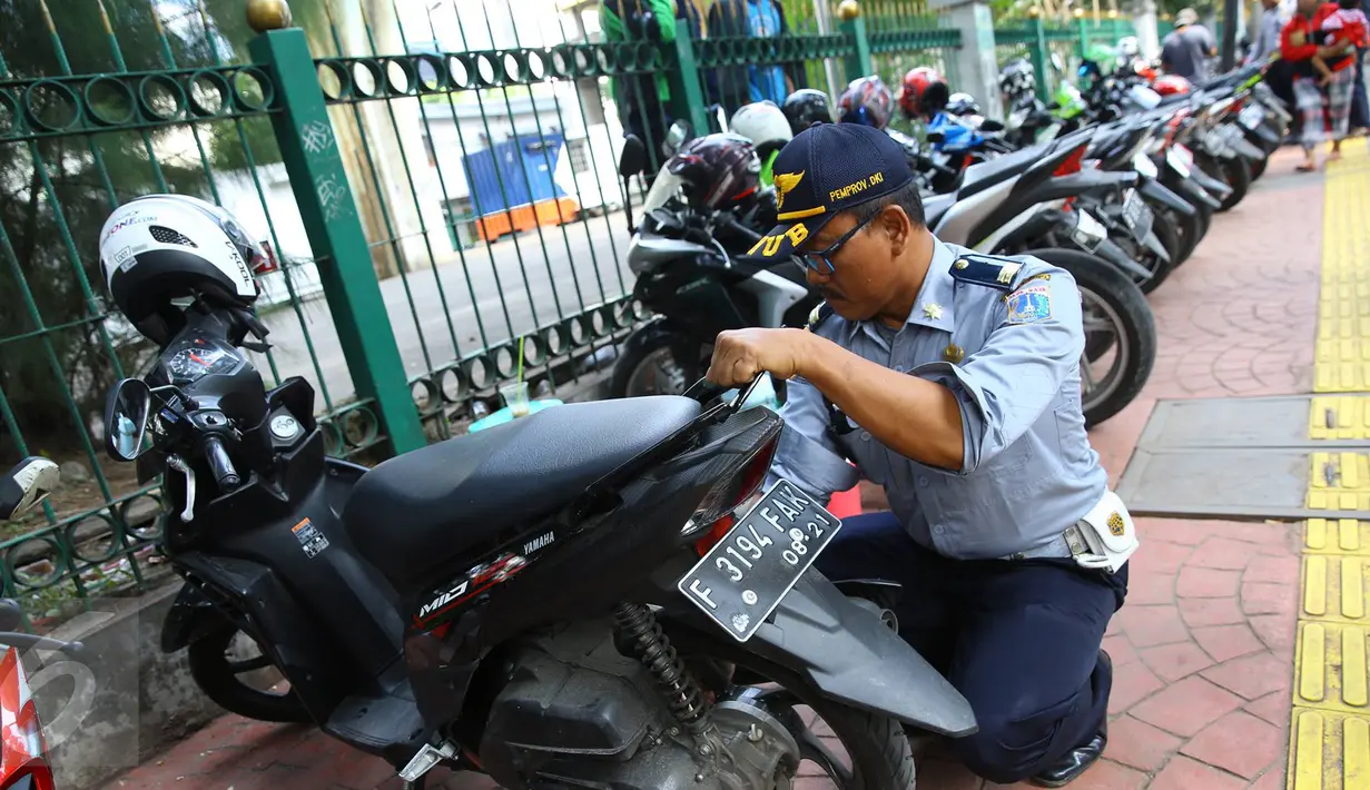 Petugas Dishub mengembosi motor yang parkir di sepanjang trotoar kawasan Kebon Sirih, Jakarta, Rabu (18/1). Puluhan motor diamankan serta digembosi dalam penertiban tersebut karena menutupi jalur pedestrian. (Liputan6.com/Immaniel Antonius)