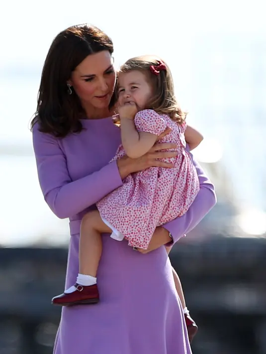 Kate Middleton menggendong sambil menghibur anaknya, Putri Charlotte, saat mengunjungi Pabrik Airbus di Hamburg, 21 Juli 2017. Putri Charlotte mendadak merajuk dan enggan naik helikopter di pabrik pesawat terbang itu. (Christian Charisius / POOL / AFP)