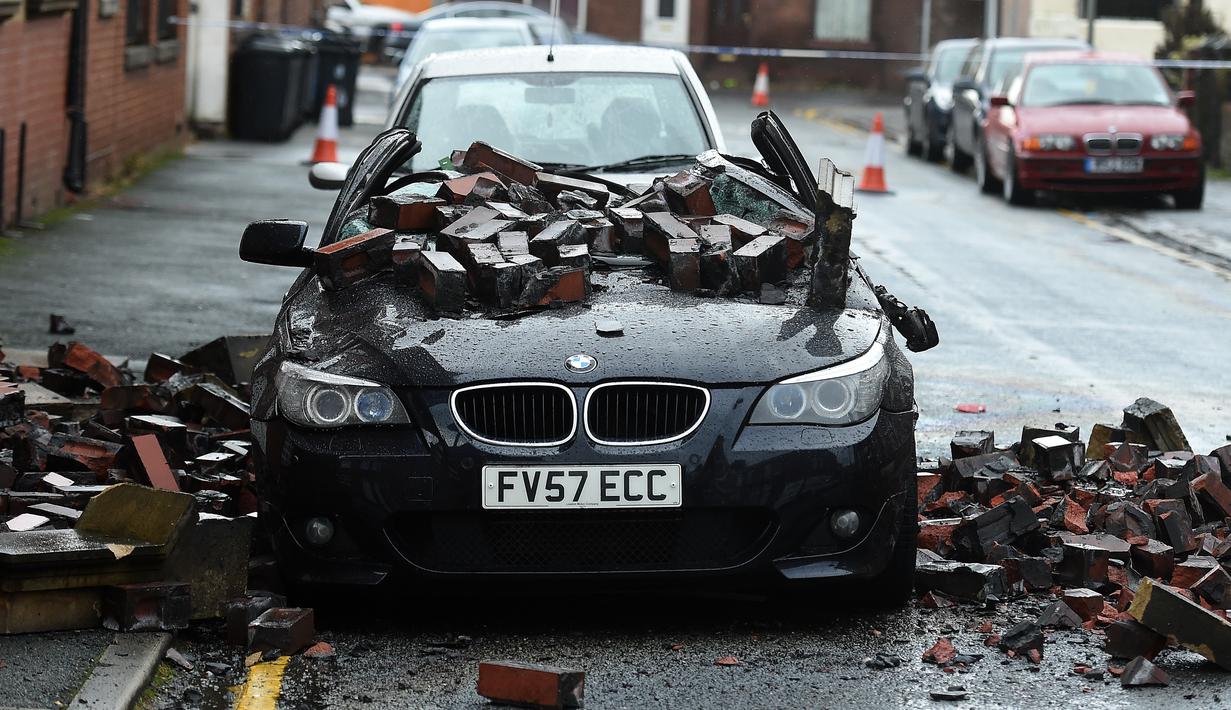 Sebuah mobil yang diparkir rusak terkena batu karena angin kencang yang disebabkan oleh atap apartemen yang runtuh di Leigh, barat laut Inggris, Rabu (18/11). (AFP PHOTO/Paul Ellis)
