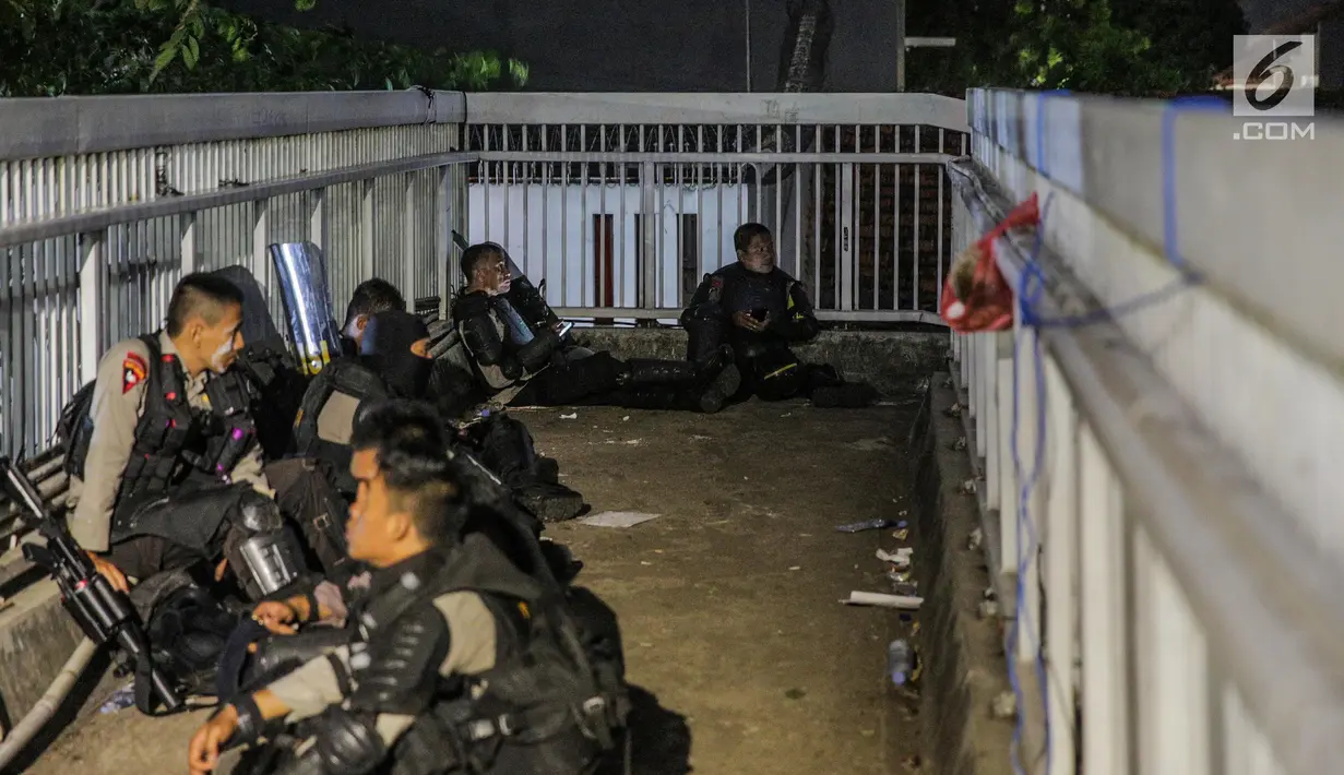 Aparat kepolisan melepas lelah di jembatan penyeberangan orang (JPO) depan Gedung DPR, Jakarta, Selasa (24/9/2019). Mereka melepas lelah usai mengawal demonstrasi mahasiswa menolak pengesahan RUU KUHP dan revisi UU KPK. (Liputan6.com/Faizal Fanani)