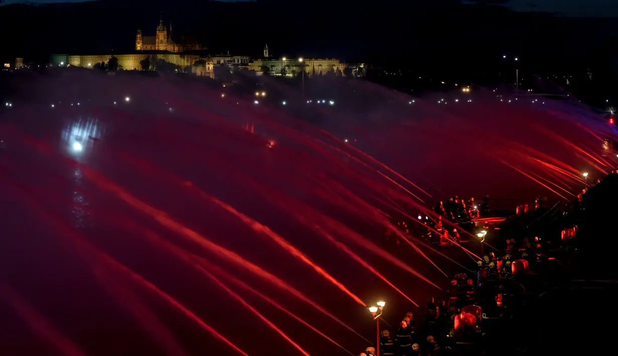 Petugas pemadam kebakaran menyemprotkan air ke Sungai Vltava berhias cahaya merah untuk menandai HUT ke-100 Ceko di Praha, Sabtu (2/6). (Michal Cizek/AFP)
