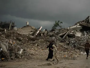 Warga Palestina berjalan melewati reruntuhan di tengah cuaca buruk Kota Gaza, Kamis 11 Desember 2025. Bencana baru mengancam ratusan ribu warga Palestina yang mengungsi di Jalur Gaza. (AP Photo/Jehad Alshrafi)