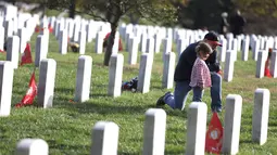 Kip Hogan didampingi putrinya mengunjungi makam temannya Army Gunnery Sgt. Terry Ball saat peringatan Hari Veteran, Arlington, Virginia, AS, Senin (11/11/2019). Rakyat AS memperingati Hari Veteran untuk menghormati mereka yang pernah bertugas di militer AS. (Alex Wong/Getty Images/AFP)