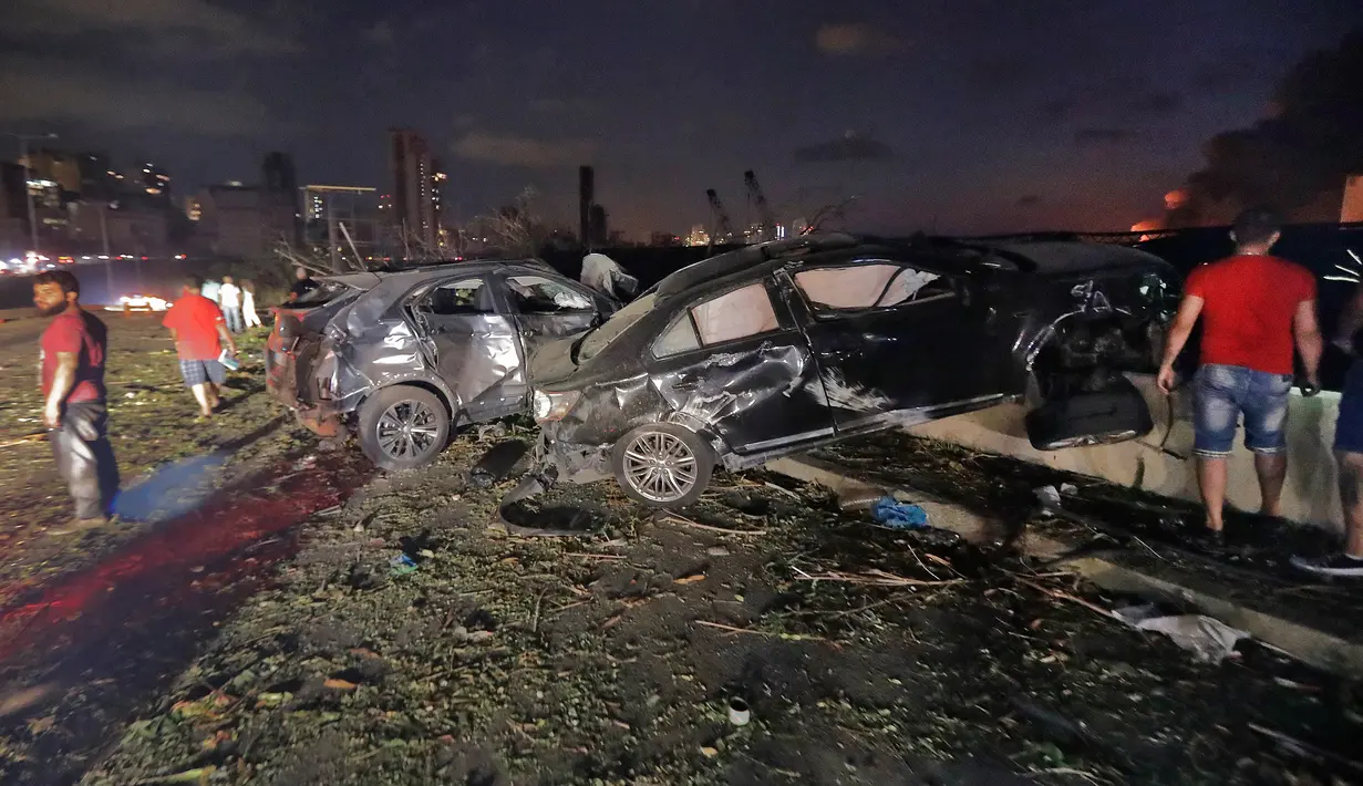 Orang-orang dekat mobil-mobil yang hancur setelah di pelabuhan Beirut, Lebanon pada Selasa (4/8/2020). Ledakan yang diduga dari gudang berisi 2.750 ton amonium nitrat meratakan hampir seluruh bangunan di sekitar Pelabuhan dan menyebabkan bangunan luluh lantak. (JOSEPH EID / AFP)