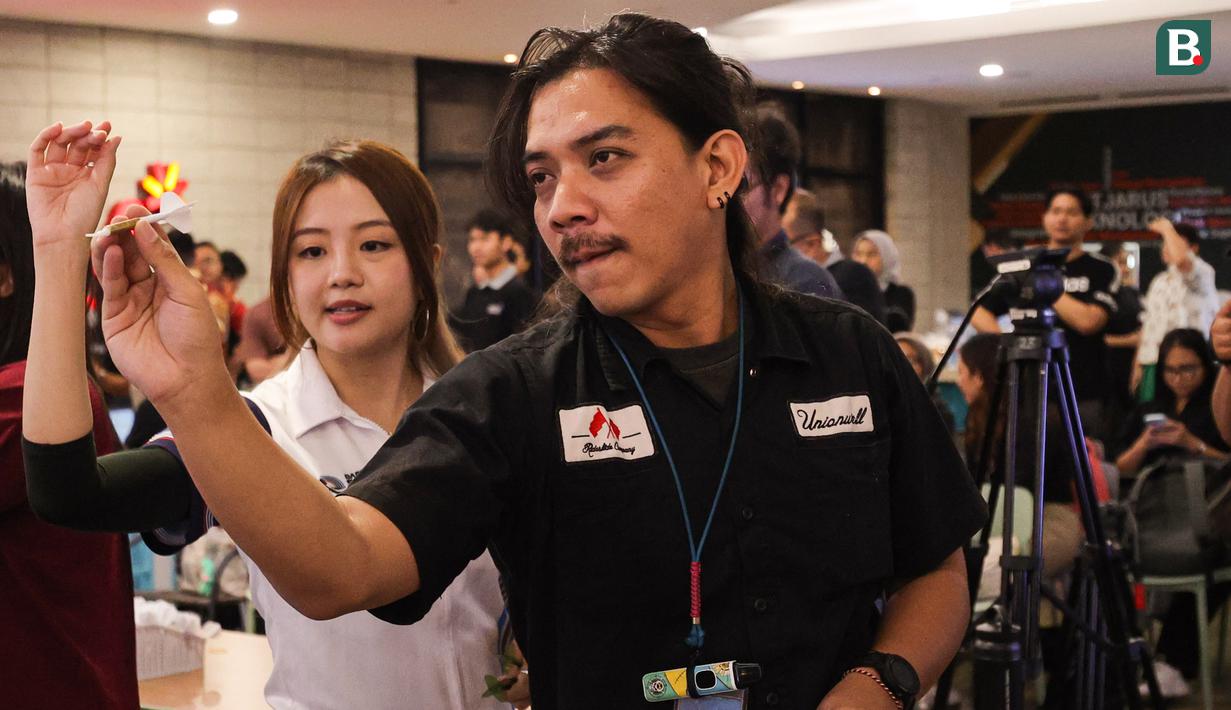 Dartslive Support Player asal Singapura Hedy Wong mengajarkan salah satu jurnalis yang mencoba alat di acara peluncuran Darts Station di lantai F7 FX Sudirman, Senayan, Jakarta pada Sabtu (15/11/2025). (Bola.com/Abdul Aziz)