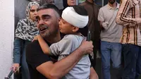 Seorang pria Palestina menggendong seorang anak laki-laki setelah dia dirawat karena cedera kepala di rumah sakit, menyusul serangan udara Israel di Rafah, di Jalur Gaza selatan pada 23 Oktober 2023. (Mohammed Abed/AFP)