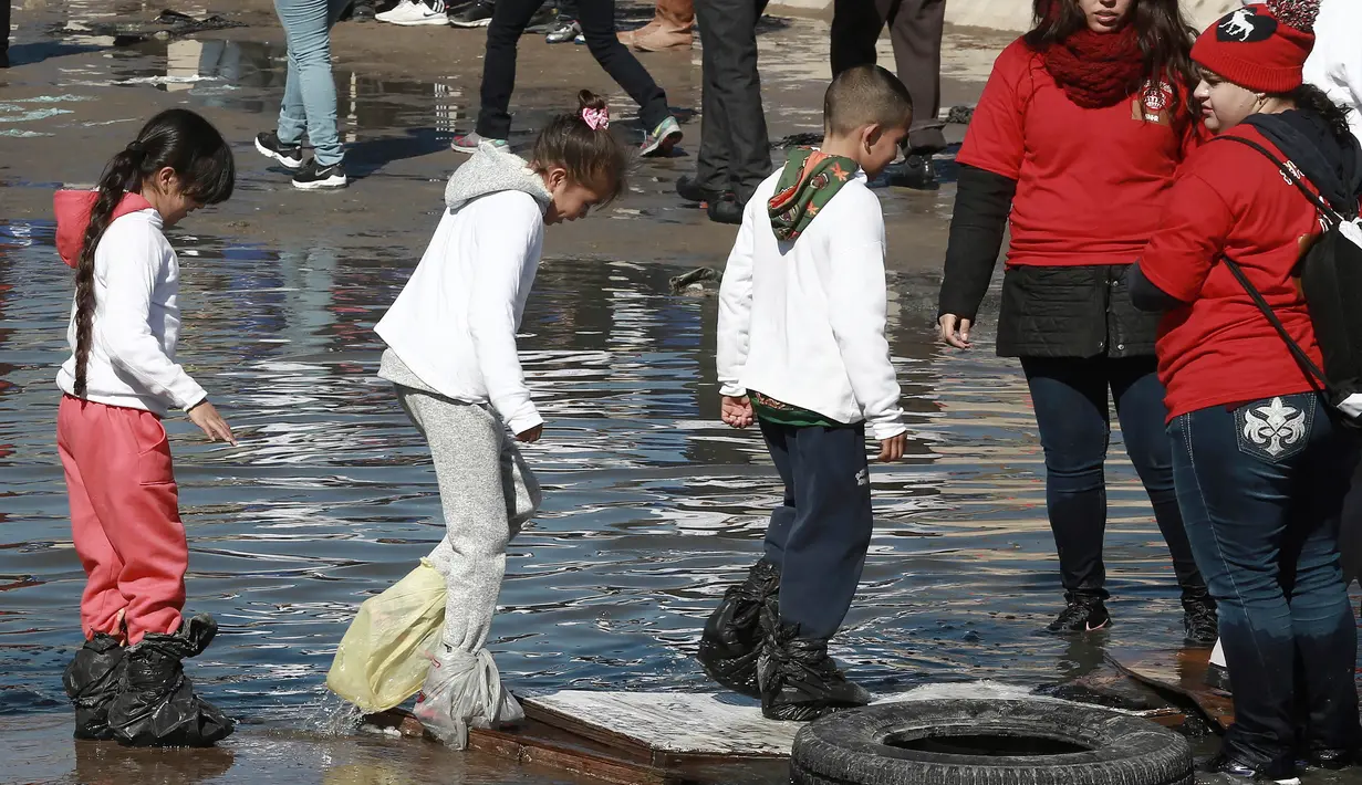 Sejumlah anak mengenakan kantong plastik untuk melindungi kakinya saat melitasi sungai untuk bertemu keluarganya di perbatasan Meksiko-AS di Ciudad Juarez, Meksiko (28/1). (AP Photo/Christian Torres)