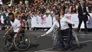 Presiden Prancis, Emmanuel Macron (tengah) bermain tenis menggunakan kursi roda bersama atlet, Michael Jeremiasz (kiri) di Paris, (24/6/2017). Kegiatan ini sebagai bentuk promosi Paris menjadi kandidat tuan rumah Olimpiade 2024. (AFP/Alain Jocard)