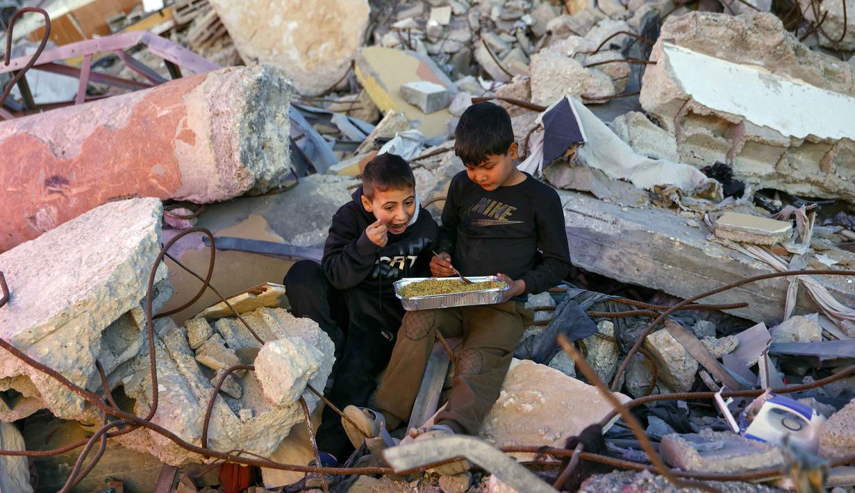Pada hari pertama Ramadan 1447 Hijriah atau Rabu (18/2/2026), mereka berkumpul untuk makan bersama sebagai simbol keteguhan dan kegembiraan di tengah kehancuran. Tampak dalam foto, anak-anak laki-laki Palestina berbagi makanan selama acara buka puasa massal yang diselenggarakan oleh Yayasan IHH Turki, di tengah reruntuhan bangunan yang hancur di Kota Gaza pada Rabu 18 Februari 2026. (Omar AL-QATTAA/AFP)