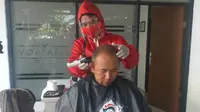 Salah satu barber aplikasi pangling tengah melayani pelanggan dengan menggunakan APD lengkap, sesuai protokoker kesehatan pencegahan Covid-19. (Liputan6.com/Jayadi Supriadin)