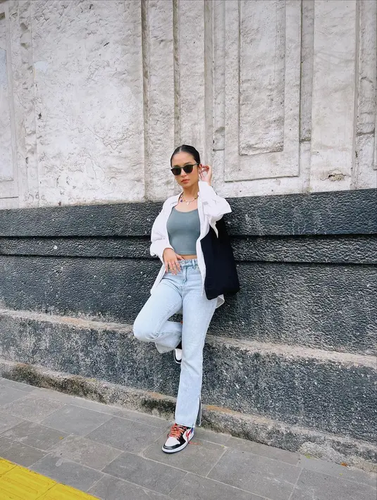 Bersandar di salah satu bangunan bersejarah, Asha Asscao terlihat santai. Meski begitu ia terlihat keren mengenakan kacamata hitam dan crop top dibalut kemeja putih.  (Liputan6.com/IG/@asha.assuncao).