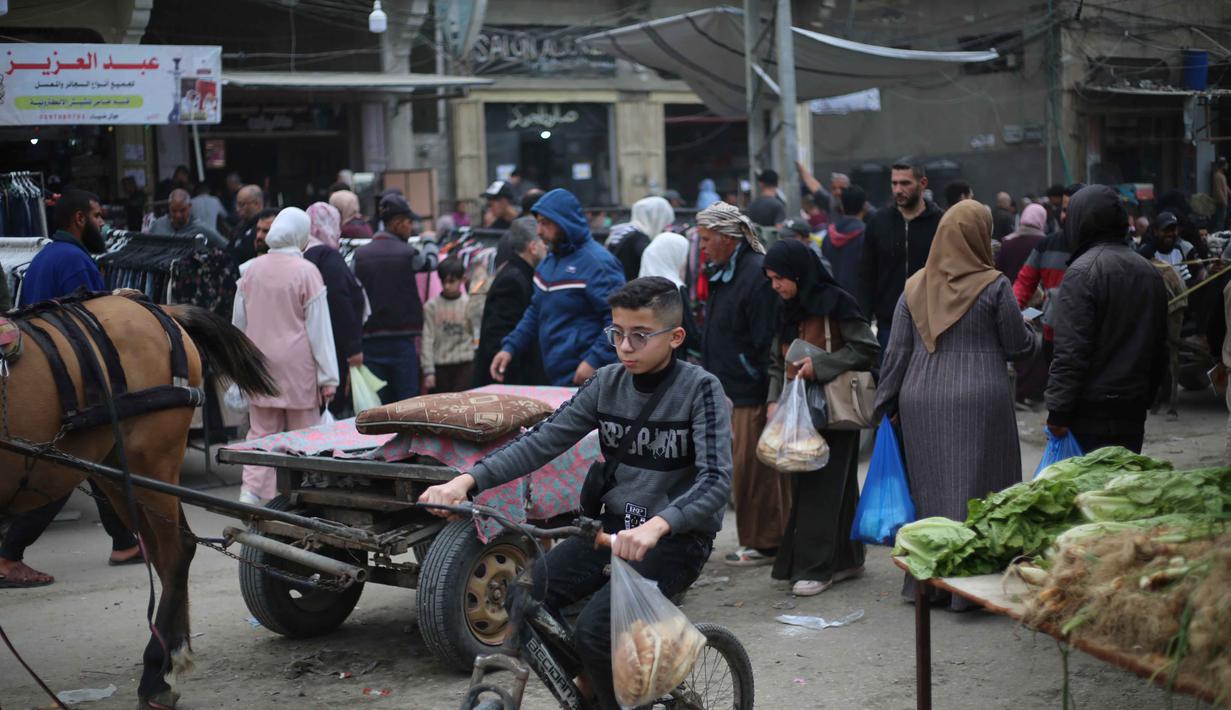 Tahun 2026 menjadi yang ketiga masyarakat Gaza merayakan Idul Fitri di tengah situasi konflik yang berkepanjangan sejak Oktober 2023. Tampak dalam foto, seorang anak laki-laki Palestina yang mengungsi mengendarai sepeda sementara orang-orang berbelanja di kios-kios di pasar jalanan sekitar kamp pengungsi Nuseirat, Jalur Gaza tengah, pada Rabu 18 Maret 2026. (Eyad Baba/AFP)