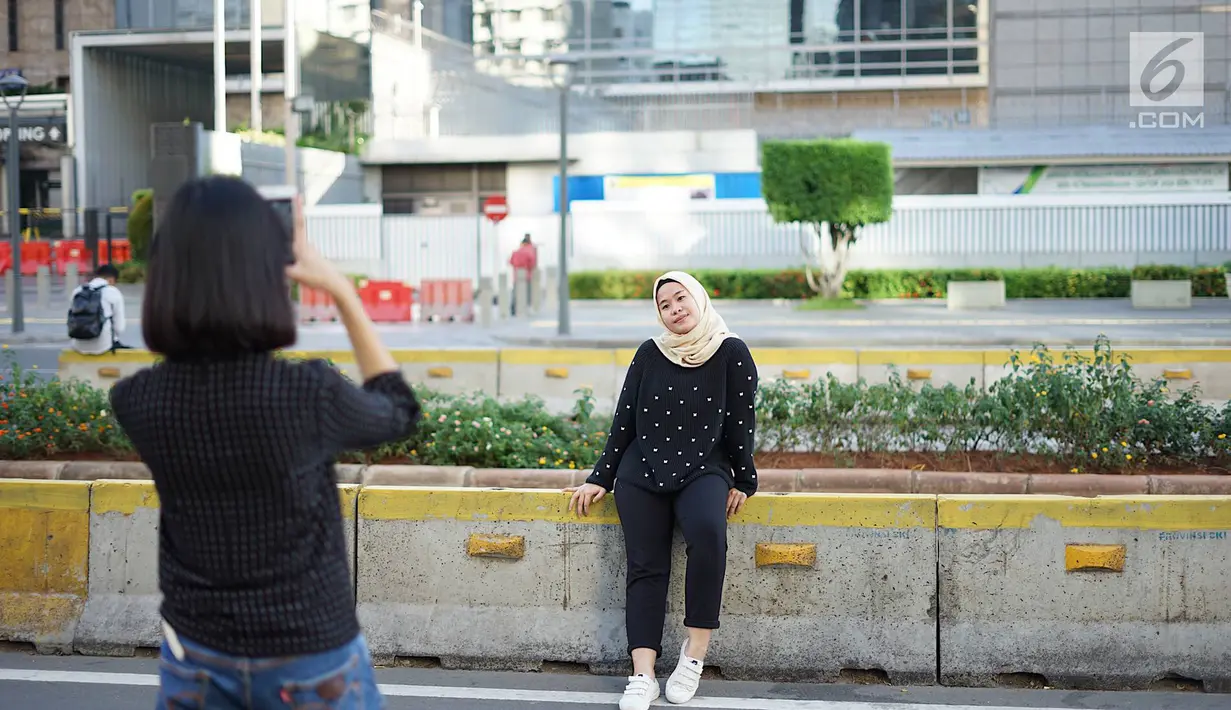 Seorang wanita berfoto dengan latar belakang Jalan MH Thamrin yang masih ditutup oleh aparat keamanan di Jakarta, Jumat (24/5/2019). Ditutupnya Jalan MH Thamrin terkait unjuk rasa menolak hasil Pemilu 2019 dimanfaatkan sebagian warga untuk berfoto. (Liputan6.com/Immanuel Antonius)