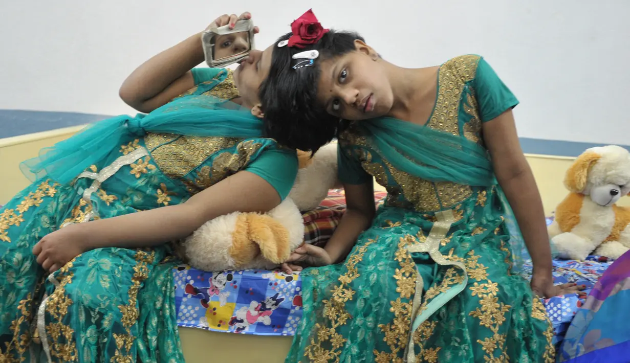 Veena (kanan) menggunakan cermin untuk melihat adiknya Vani saat berada di Rumah Anak di Hyderabad, India (2/1). Veena dan Vani adalah kembar siam dengan kepala yang menempel.  (AFP/Noah Seelam)