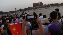 Warga mengambil foto setelah upacara pengibaran bendera saat fajar setelah kematian mantan perdana menteri China Li Peng di Lapangan Tiananmen Beijing (24/7/2019). Li Peng meninggal dunia akibat menderita kanker kandung kemih. (AFP Photo/Greg Baker)