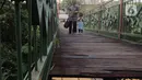 Seorang ibu bersama anak kecil melintasi jembatan yang berlubang di Jembatan Wiratman, Srengseng Sawah, Jakarta, Sabtu (12/3/2022). Jembatan tersebut menghubungkan Kelurahan Srengseng Sawah, Jakarta Selatan dengan Kelurahan Pasir Gunung Selatan, Depok. (Liputan6.com/Herman Zakharia)