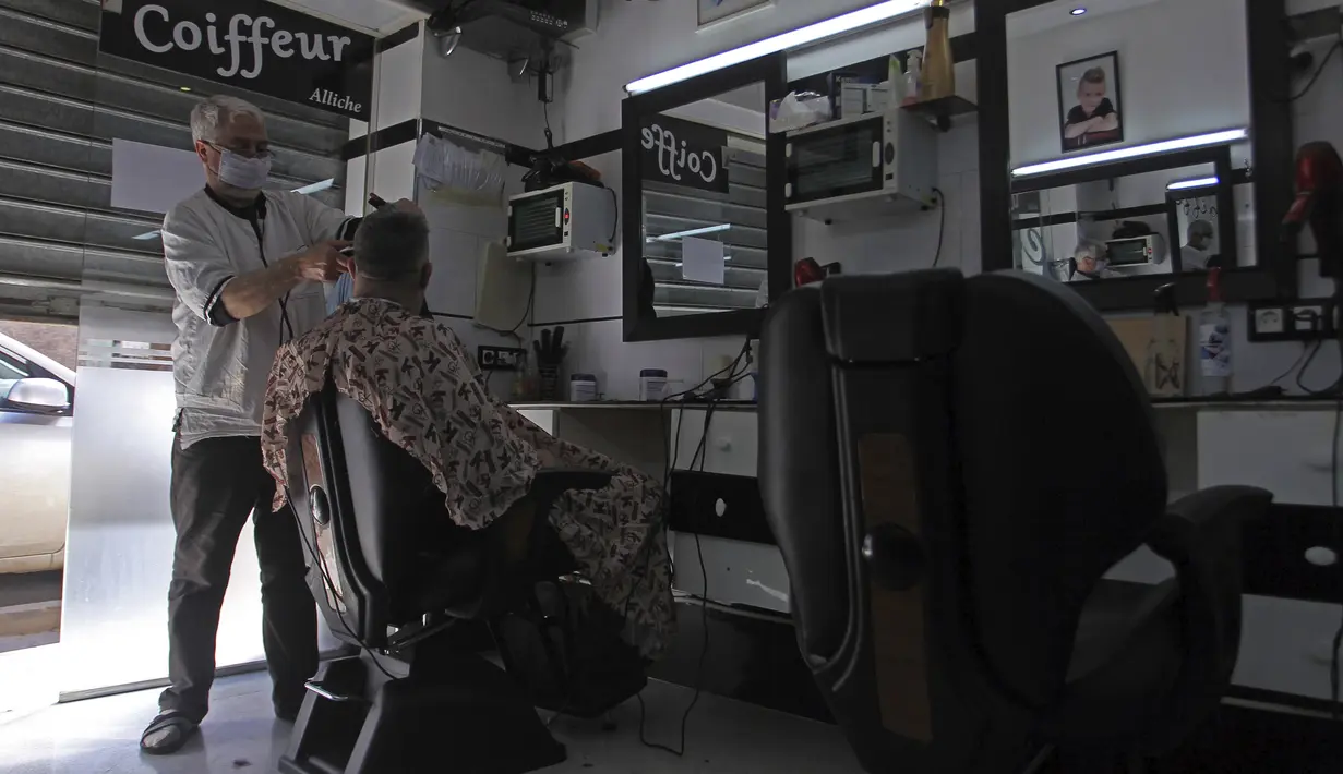 Tukang cukur memotong rambut pelanggannya di Algiers, Aljazair, Rabu (29/4/2020). Aljazair melonggarkan langkah-langkah karantina akibat virus corona COVID-19 sejak hari pertama bulan suci Ramadan dengan memperpendek jam malam dan memungkinkan beberapa kegiatan komersial. (AP Photo/Fateh Guidoum)