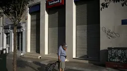 Seorang wanita melintas di depan sebuah bank yang berhenti beroperasi di Athena, Yunani, (29/6/2015). Seperti dikutip BBC, penarikan uang pun dibatasi hanya 60 euro per hari. (REUTERS/Alkis Konstantinidis)