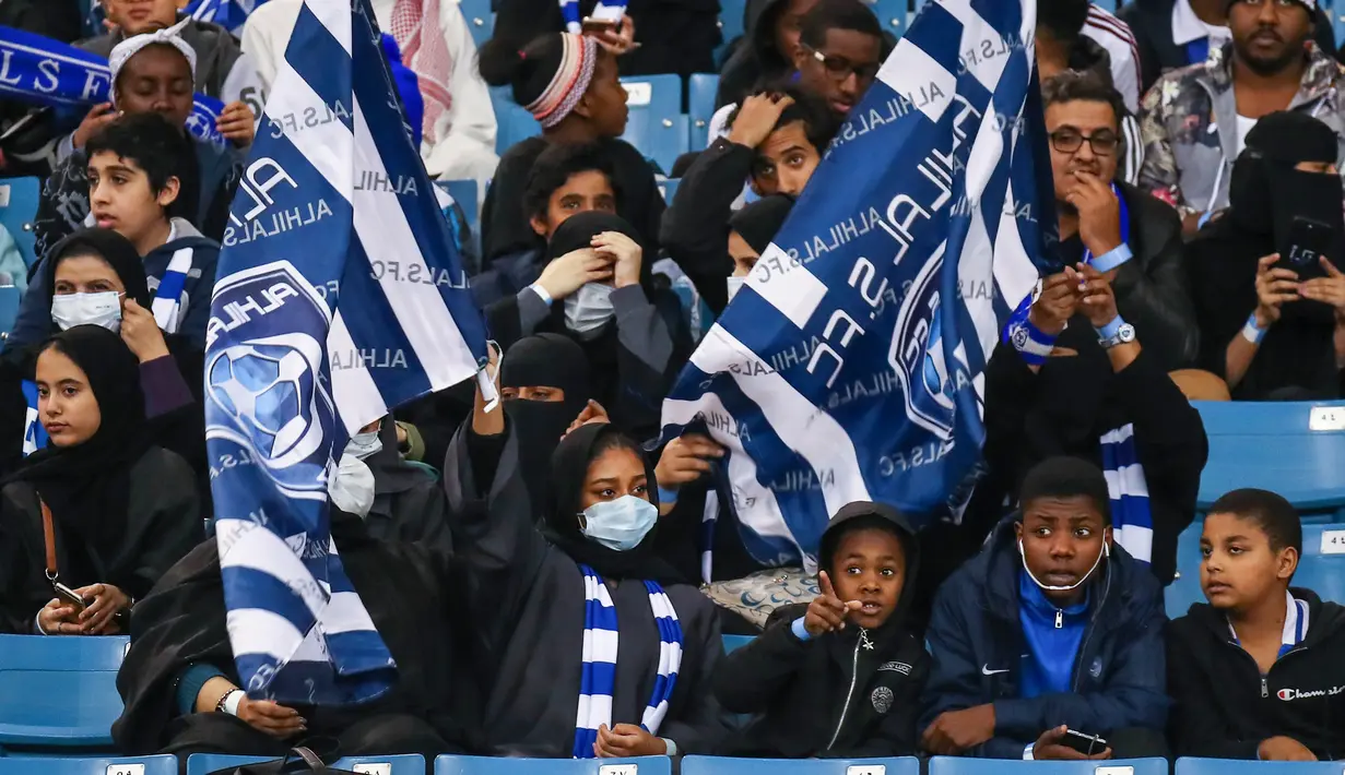 Sejumlah pendukung wanita Al-Hilal mengibarkan bendera saat mendukung timnya dalam pertandingan Liga Saudi Pro di Riyadh (13/1). Arab Saudi untuk pertama kalinya mengizinkan wanita memasuki stadion sepak bola. (AFP Photo/Ali Al-Arifi)