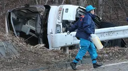 Seorang penyidik berjalan di dekat bangkai bus yang tergelincir di Karuizawa, prefektur Nagano, Jepang, Jumat (15/1). Bus yang membawa pengunjung resor ski itu tergelincir dan menewaskan 14 orang serta melukai 27 lainnya. (AFP PHOTO/Jiji Press JAPAN OUT)