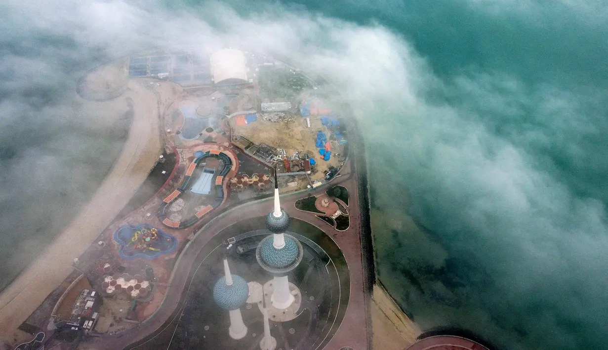 Kuwait Towers saat pagi berkabut di Kota Kuwait terlihat dalam foto udara, Selasa (14/3/2023). Terlihat gedung-gedung pencakar langit menembus awan yang seakan-akan seperti kota langit. (Photo by Yasser Al-Zayyat / AFP)