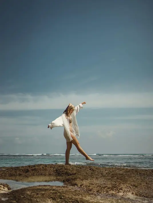 Terlihat riang, Pamela Bowie berpose di bebatuan pinggir pantai mengenakan two-pieces bikin yang seragam dengan scarf yang dipakainya sebagai bandana. Terlihat Pamela juga mengenakan oversized white shirt. Foto: Instagram.