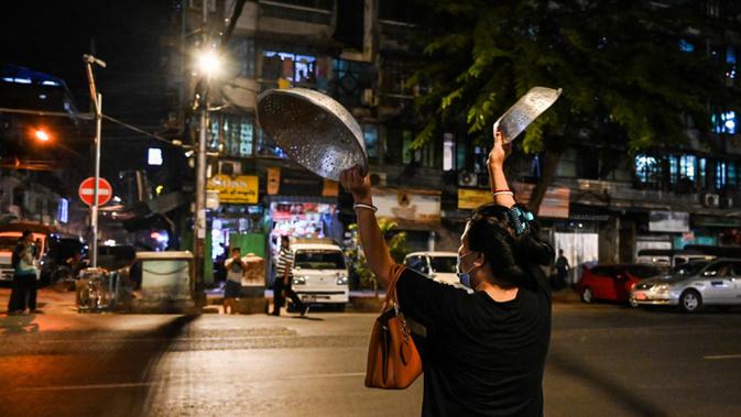 Seorang wanita membuat keributan dengan memukul-mukul panci setelah seruan untuk protes keluar di media sosial di Yangon, Myanmar, 3 Februari 2021. Kudeta militer Myanmar terus memicu protes warga dengan membunyikan klakson mobil, menyalakan lampu ponsel, dan memukul-mukul panci. (STR/AFP)