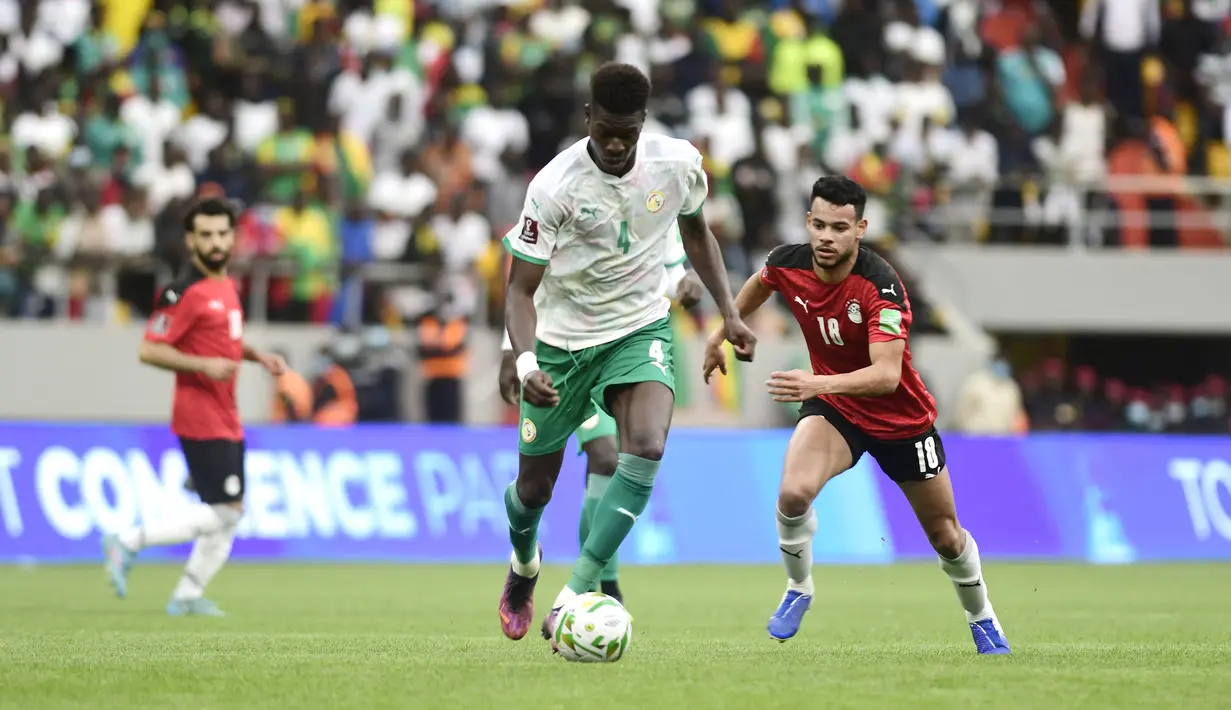 Bek Pape Abou Cisse berebut bola dengan gelandang Mesir Nabil Dounga pada Kualifikasi Piala Dunia 2022 zona Afrika di Stade Me Abdoulaye Wade, Rabu (30/3/2022) dini hari WIB. Senegal dipastikan lolos ke Piala Dunia 2022 setelah menang adu penalti atas Mesir 3-1. (SEYLLOU / AFP)