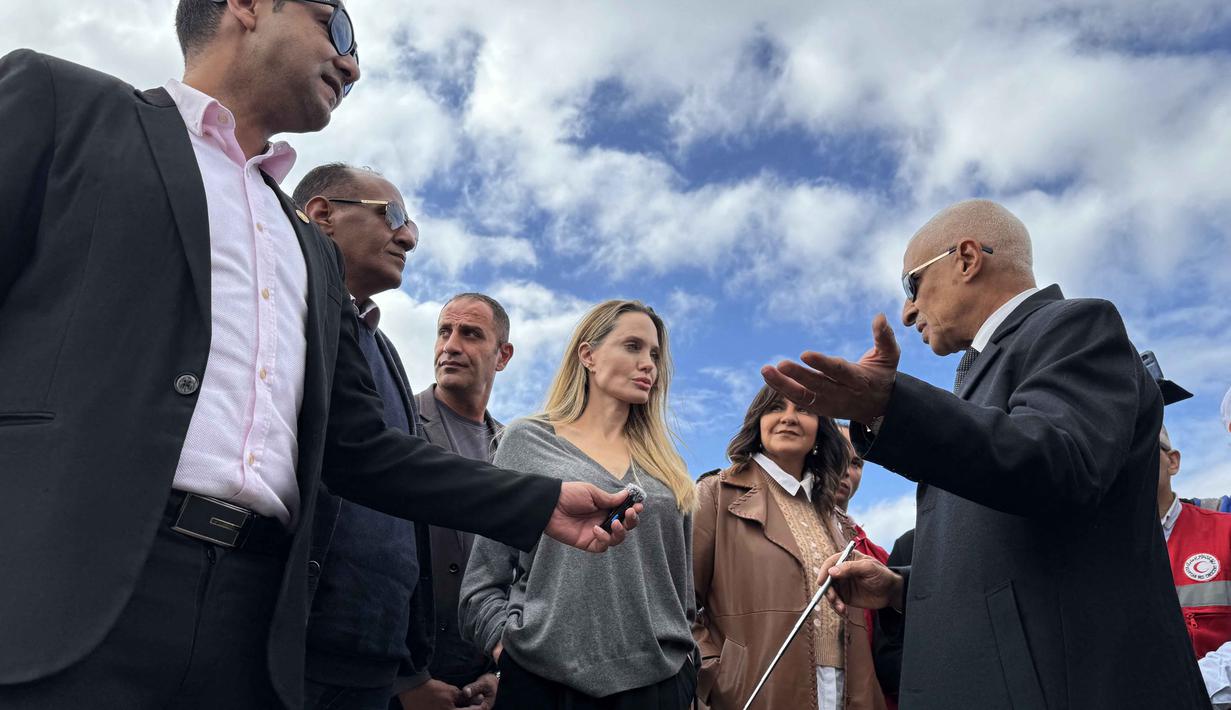 Kunjungan Angelina Jolie terjadi ketika Israel mengatakan akan menangguhkan operasi puluhan kelompok bantuan yang bekerja di Jalur Gaza. Tampak dalam foto, aktris Amerika Serikat (AS), Angelina Jolie (ketiga kanan) berbicara dengan seorang pejabat di perbatasan Rafah Mesir, pada Jumat 2 Januari 2026. (Foto oleh AFP)